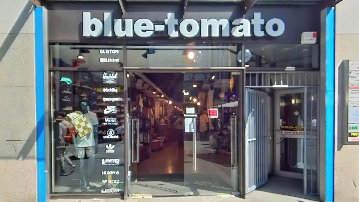 Blue Tomato Shop mit blauer Markise zwei großen Fenstern mit Kleidung an Straße mit anderen Geschäften Bekleidungsgeschäft Köln Neumarkt-/Cäcilien-Viertel