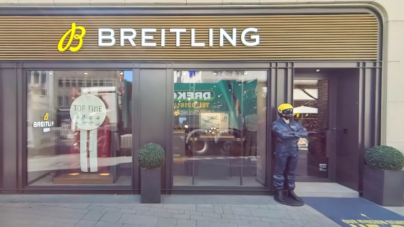 Breitling Boutique mit goldenem Logoschild Topfpflanzen am Eingang Uhrenauslagen Person mit Helm davor Uhren Köln City