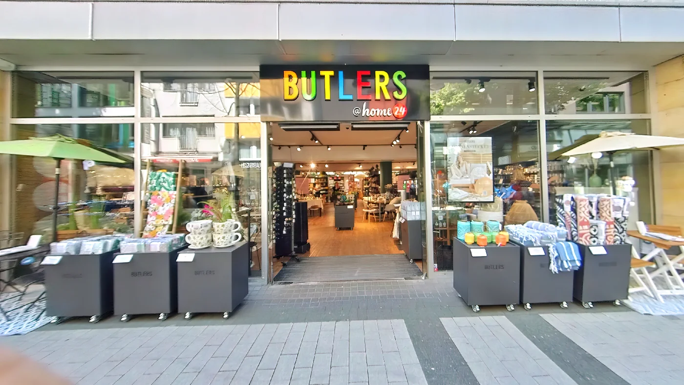 BUTLERS in Breite Straße Fassade mit schwarzem Vordach gelb-weißem Namen vier Mülltonnen davor Fensterauslagen Einrichtung Köln Neumarkt-/Cäcilien-Viertel
