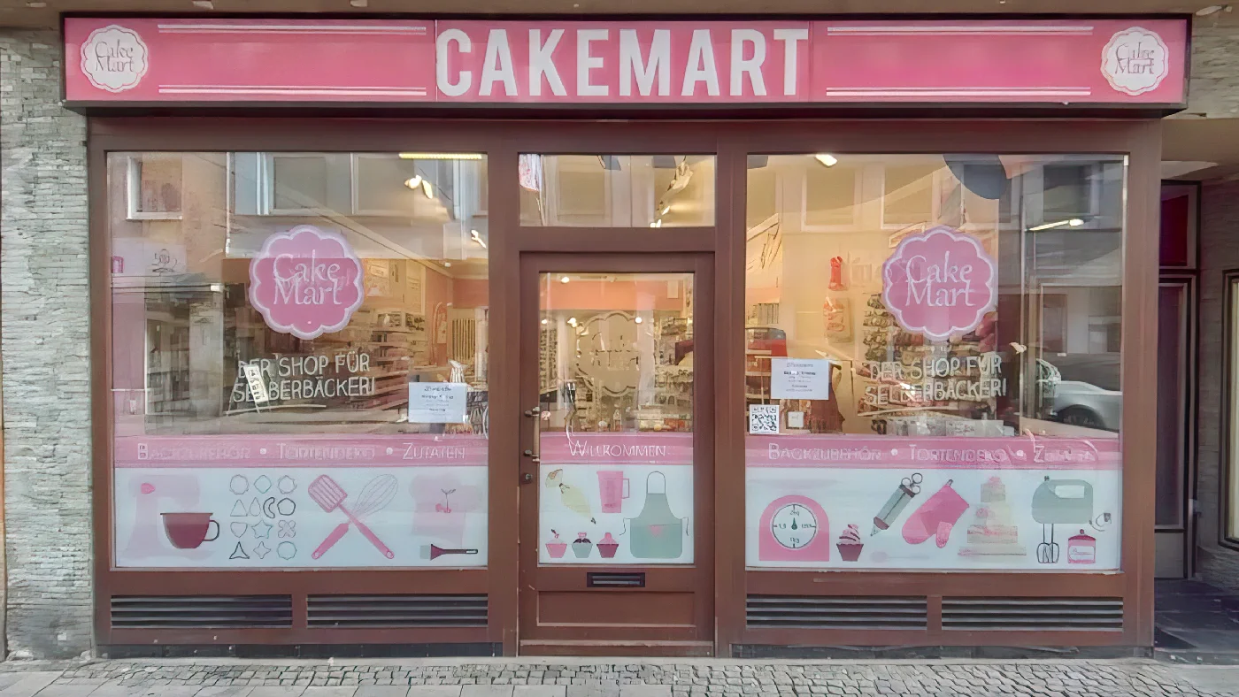 Cake Mart Geschäft mit rosa-roter Fassade Aufklebern mit Motiven Schildern für Backzubehör an Kopfsteinpflasterstraße Divers Köln Severins-Viertel