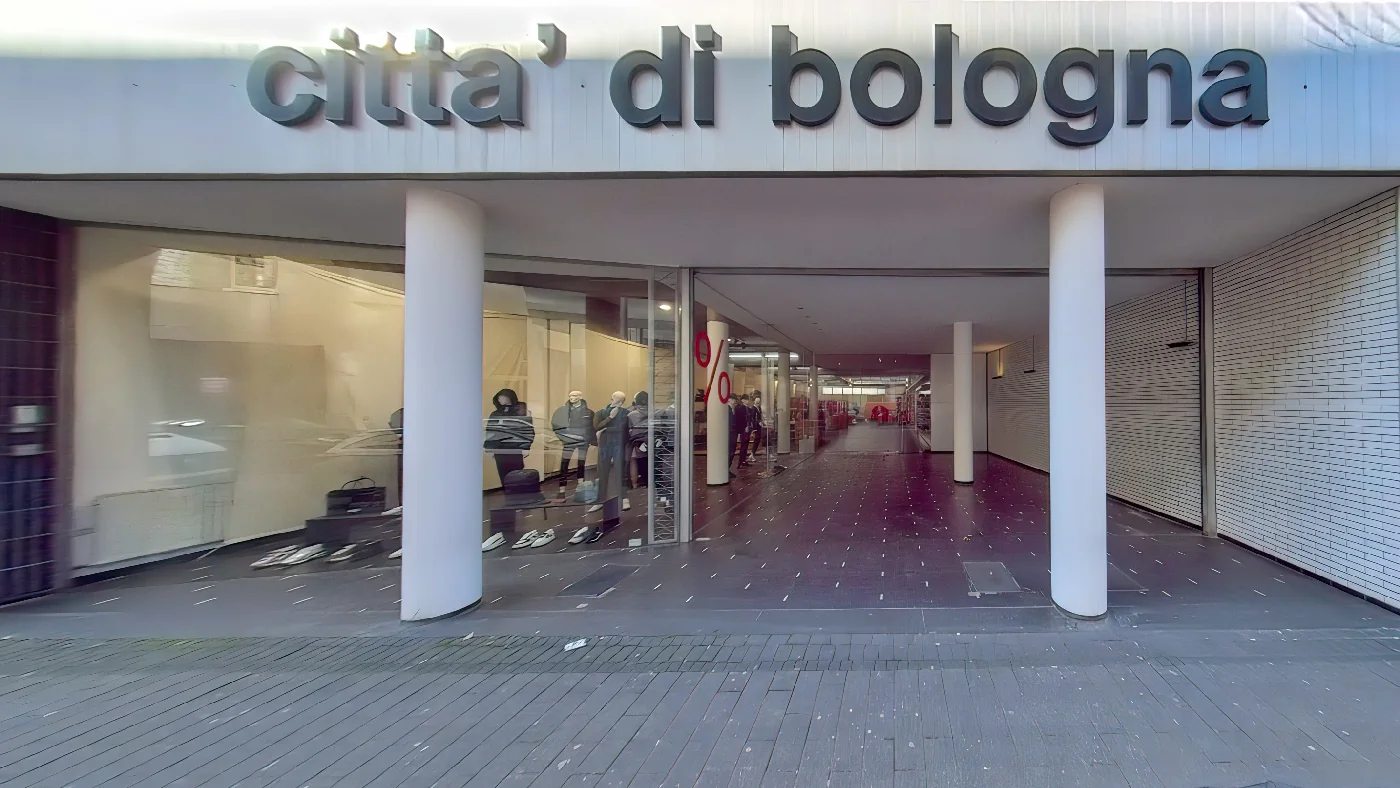 Einkaufszentrum Città di Bologna Italien überdachter weißer Eingang Säulen Decke graue Fliesen Leute offene Geschäfte Kleidung linker geschlossen Rollladen rechts Herrenmodengeschäft Köln Belgisches Viertel