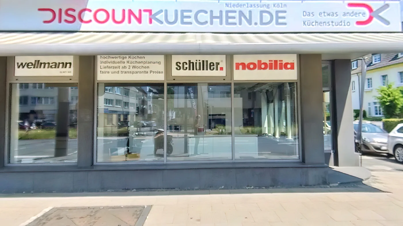 Schaufenster Geschäft Discount Küchen in Köln Markennamen auf Fenster Schild "Das etwas andere Kuechenstudio" draußen mit blauem Himmel und Bäumen Küchenmöbel Köln Braunsfeld