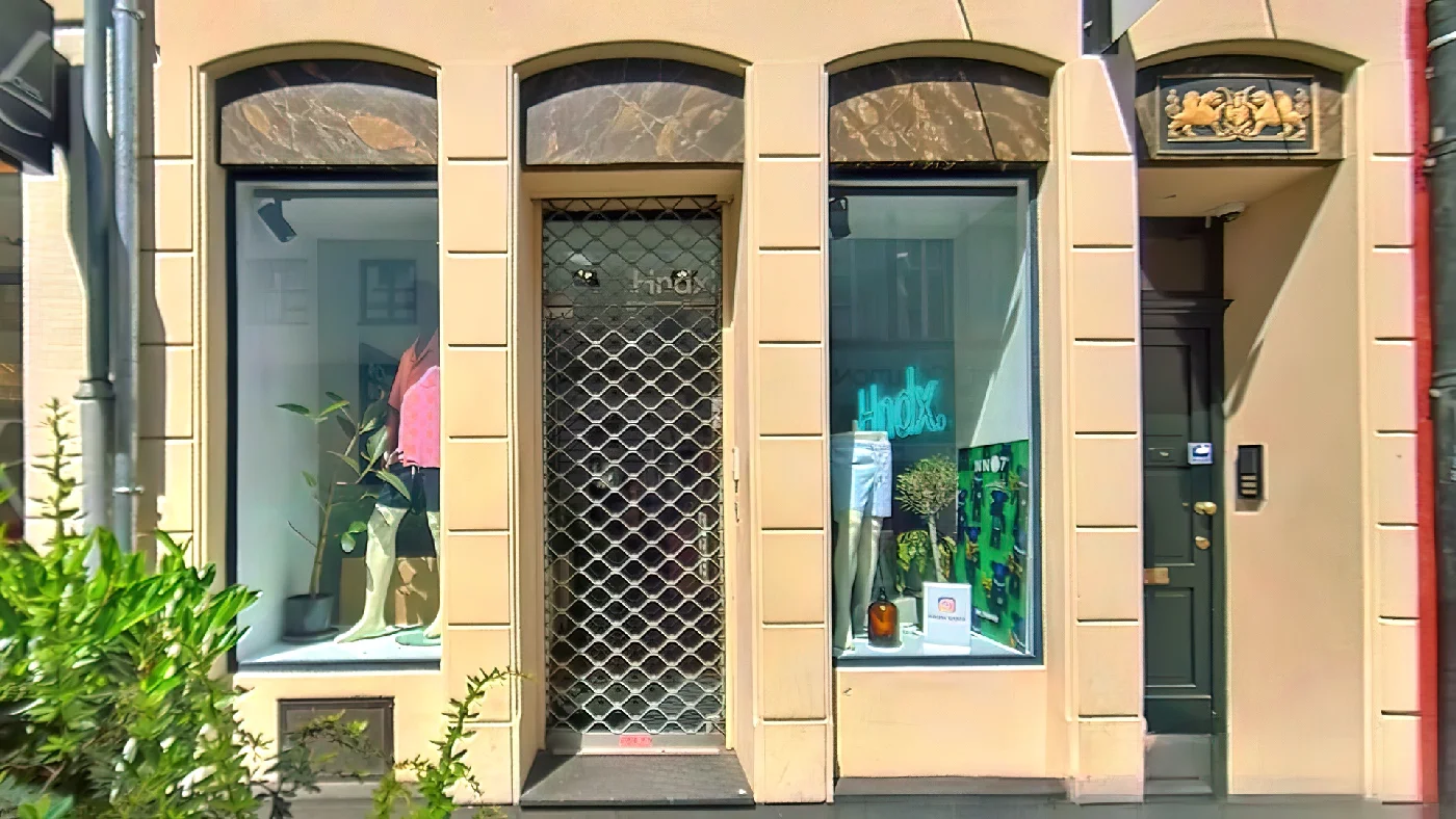 Hndx Geschäft hellbeige Fassade mit rotem Rand Bogenfenster mit Kleidung Metallgitter Pflanzen. Herrenmodengeschäft Köln Apostel-Viertel