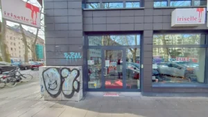 Iriselle: rote Markise graue Fassade Verkaufsschild Fahrrad vor Geschäft Graffiti. Damenmodengeschäft Köln Rathenau-/Komponistenviertel