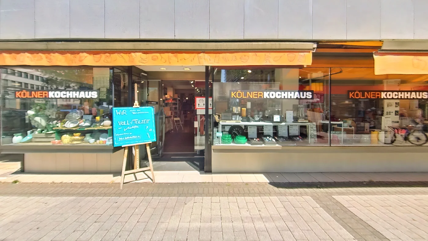 Kölner Kochhaus-Geschäft mit orangefarbenem Vordach Schaufenster mit Namen Eingangstür mit rotem Schild. Fachhandel für Küchenbedarf Köln City
